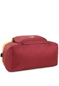 Bolso de deporte en rojo y amarillo, hecho de nylon. Forma rectangular con cierre de cremallera en la parte superior. Cuenta con un pequeño parche de logo en el frente.