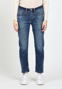 Dunkelblaue Denim-Jeans mit geradem Schnitt, ausgestattet mit fünf Taschen, sichtbaren Nähten und einem Knopfverschluss. Getragen mit weißen Sneakern.