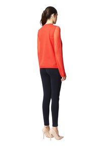 Maglia rossa a maniche lunghe con scollatura a girocollo, abbinata a leggings neri e scarpe con tacco nude. Tessuto liscio con una silhouette aderente.