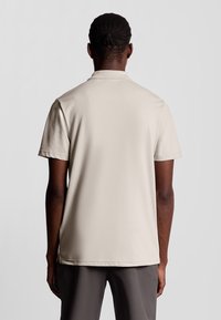 Beige katoenen polo shirt met een standaard kraag en korte mouwen, met een eenvoudig ontwerp en geen zichtbare logo's of patronen op de achterkant.