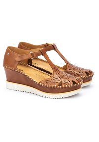 Scarpe con zeppa in pelle marrone con design perforato, fascetta a T e suola in gomma bianca. Presentano dettagli cuciti lungo i lati.