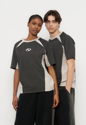 Δύο νεαροί ενήλικες φοράνε ταιριαστά γκρι πουκάμισα δύο τόνων και μαύρο παντελόνι, στέκονται κοντά σε απλό λευκό φόντο.