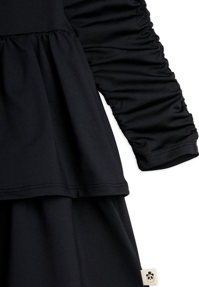 Μαύρο φόρεμα με μακριά ρυχά μανίκια, στρωμένη κοπή peplum, μαλακό ελαστικό ύφασμα και μια μικρή ετικέτα panda στο τελείωμα.