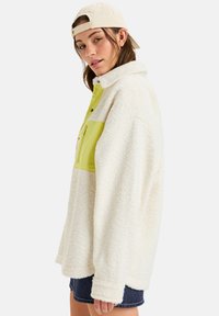 Fleece-Pullover in Creme mit einem leuchtend grünen Einsatz; verfügt über einen hohen Kragen, einen Knopfverschluss und kontrastierende Farben. Weicher Stoff, oversize Passform.