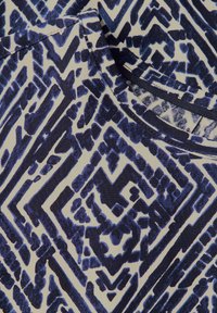 Tessuto a righe blu navy e bianco con geometrie e linee. La texture sembra liscia con una leggera lucentezza. Design a scollo rotondo.
