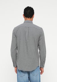 Karierte langärmelige Bluse in Schwarz und Weiß, mit einem strukturierten Kragen und Knopfdetails, aus leichtem Stoff mit einer glatten Textur.