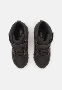 Black waterproof boots with a textured fabric upper, padded collar, and durable rubber sole. Features elastic laces and a hook-and-loop strap.