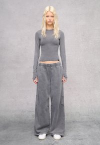Maglietta grigia a maniche lunghe e pantaloni larghi in felpa realizzati in tessuto morbido. I pantaloni presentano una vita elastica; il modello indossa sneakers bianche.