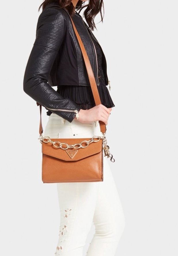 Tan læder crossbody taske med et trekantet logo, kædetræk og et fladt design, båret af en person iført en sort jakke og hvide bukser.