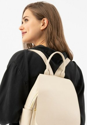 Beige leren rugzak met een gestructureerd ontwerp, afgeronde bovenkant en een textuurafwerking. Voorzien van verstelbare riemen en een klein voorvak met rits.