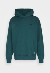 Sudadera verde azulado oscura, hecha de tela suave, con un bolsillo canguro, puños acanalados y un pequeño logo negro en el pecho.
