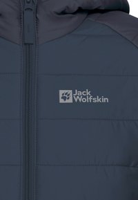 Marinblå isolerad jacka med quiltat mönster, har dragkedja och en kontrasterande krage. Logotypen "Jack Wolfskin" tryckt på framsidan.