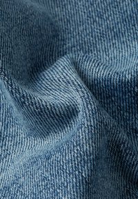 Tissu en denim bleu avec une texture douce, présentant un motif de toile sergée classique et des nuances de bleu variées.
