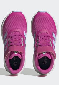 Zapatillas deportivas rosas hechas de malla texturizada, con una correa gris y tres rayas blancas a cada lado. Suelas de goma redondas.