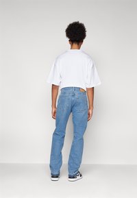 Camiseta blanca de gran tamaño y jeans rectos de color azul claro. Los jeans tienen bolsillos traseros y un parche de cuero marrón en la cintura.
