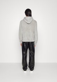 Felpa grigia con cappuccio e vestibilità comoda, abbinata a pantaloni neri lucidi e testurizzati con motivo a pelle di coccodrillo e sneakers bianche.