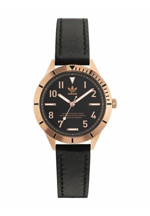 Montre avec bracelet en cuir noir et boîtier en or rose, cadran noir, grands marqueurs d'heure et logo adidas. Présente un bracelet texturé et un design simple.