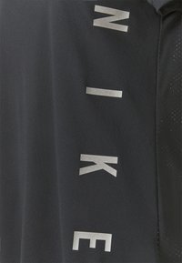 Svart träningsskorta med stora vita "NIKE"-bokstäver på sidan, tillverkad av mjukt tyg med en lätt glans och en sportig design.