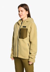 Beige Fleecejacke mit Kapuze, ausgestattet mit einem Reißverschluss und einer olivgrünen Brusttasche. Strukturiert mit einer weichen Oberfläche.
