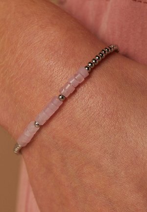 Perlenarmband mit durchsichtigen, rosa rechteckigen Perlen und metallischen, silbernen, sphärischen Akzenten, am Handgelenk mit sichtbarer Hautstruktur getragen.