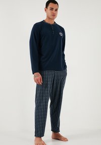 Námořnická modrá noční košile s dlouhým rukávem a zapínáním na knoflíky, s logem na hrudi, v kombinaci s kostkovanými námořnickými pyžamovými kalhotami vyrobenými z měkké tkaniny.