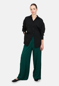 Black button-up shirt with a collar and long sleeves, paired with flowy green wide-leg pants. Black flat shoes complete the outfit.