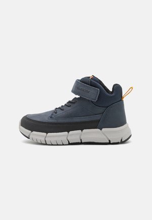 Sneakers blu a mezza altezza con tomaia in suede e mesh liscia, fissati con una fascia in velcro, suola in gomma e suola grigia a contrasto.