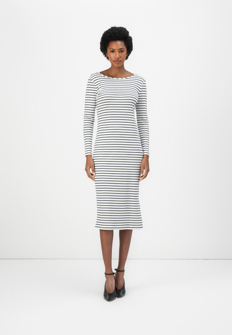 Robe ajustée à manches longues avec des rayures horizontales noires et blanches, encolure ronde, longueur genoux, fabriquée en tissu doux, associée à des talons noirs.