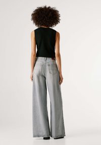 Μαύρο αμάνικο πλεκτό τοπ συνδυασμένο με ανοιχτό γκρι τζιν παντελόνι ψηλόμεσο, με φαρδύ πόδι. Ορατές πίσω τσέπες και δερμάτινη ετικέτα της μάρκας στη μέση.
