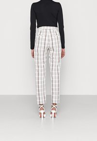 Bílé kostkované kalhoty s hnědými akcenty, vysokým pasem a rovnými nohavicemi. V kombinaci s černým topem s dlouhým rukávem a bílými sandály na vysokém podpatku.