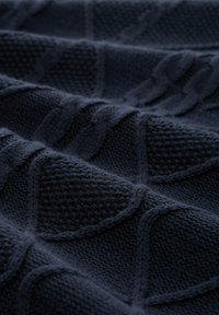 Tissu tricoté bleu marine présentant des motifs de câbles texturés avec des points en relief, créant de la profondeur et une variation tactile à travers le textile.