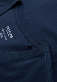 Camiseta de algodón azul marino con un cuello redondo. Las características incluyen una textura suave, costuras a lo largo de los bordes y una etiqueta con información de la marca.