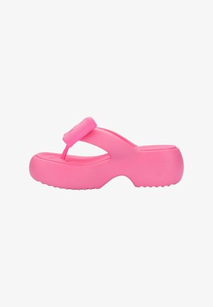Różowa gumowa klapka z podniesionym paskiem między palcami i grubą platformową podeszwą. Gładka faktura i zaokrąglone krawędzie tworzą minimalistyczny wzór.