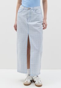 Gonna maxi in denim a righe blu e bianche con uno spacco frontale, dotata di chiusura a bottoni e tasche. Abbinata a sneakers bianche.