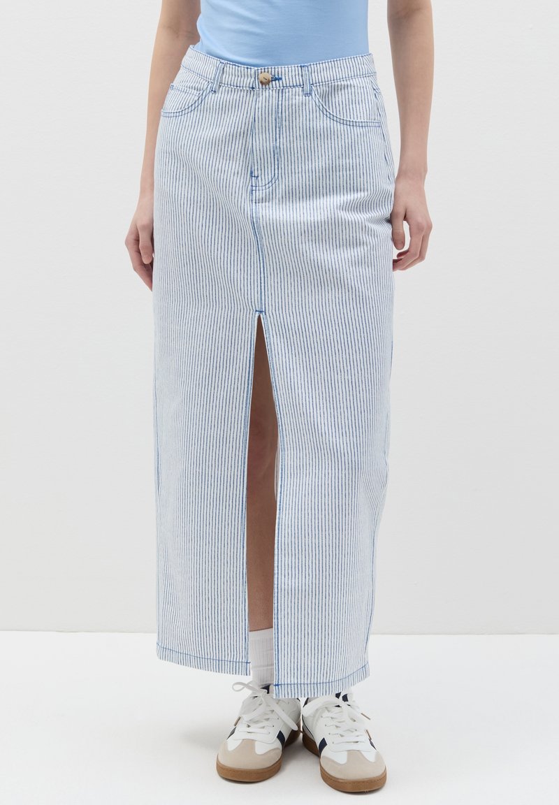 Gonna maxi in denim a righe blu e bianche con uno spacco frontale, dotata di chiusura a bottoni e tasche. Abbinata a sneakers bianche.