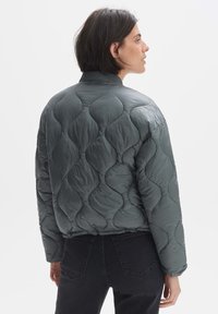 Gevoerde, donkergrijze jas met een gequilt patroon en een ribbelkraag. Heeft een relaxte pasvorm en een gestructureerd oppervlak voor warmte. In combinatie met zwarte jeans.