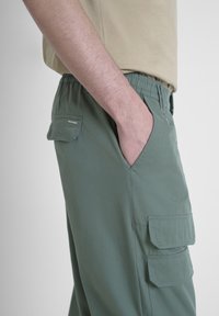 Groene cargobroek met een elastische tailleband, zijzakken en een opgestikte zak op de dij. Gemaakt van lichtgewicht stof met een gladde textuur.