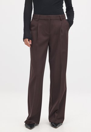 Pantalones marrones a medida con cintura alta, textura suave, piernas anchas y pliegues frontales, combinados con un top negro ajustado de manga larga.