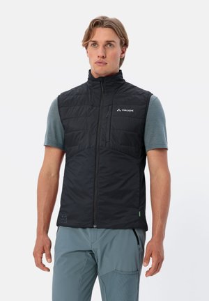 Gilet isolato nero con colletto alto, chiusura con zip e design trapuntato. Presenta una tasca sul petto sinistro e un dettaglio del logo. Indossato sopra una camicia teal.