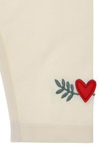 Cremfarbene Hose mit grünem, gesticktem Blätterdesign und rotem Herzakzent am Saum. Weicher Baumwollstoff, figurbetonte Passform.