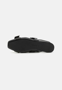 Zapato negro con textura suave, con punta redondeada y dos correas ajustables. La suela tiene un patrón de relieve claro para un mejor agarre.
