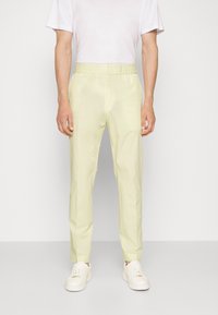 Ljust gula, byxor med elastisk midja och smal passform, kombinerade med vita sneakers och en enkel vit t-shirt. Slät textur.
