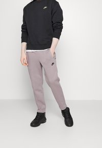 Sudadera negra de cuello redondo con el logo dorado de Nike, pantalones de chándal gris claro ajustados con el logo negro de Nike y zapatillas negras. Textura suave.