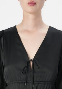 Vestido de cetim preto com um decote em V profundo, detalhe de laço na gola e mangas bufantes com uma cintura franzida.