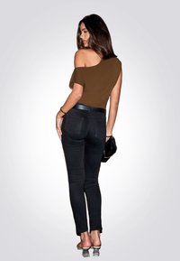 Braunes Off-Shoulder-Oberteil, schwarze eng anliegende Jeans und transparente Blockabsatzsandalen. Dazu gehören ein Armband und eine kleine schwarze Clutch.