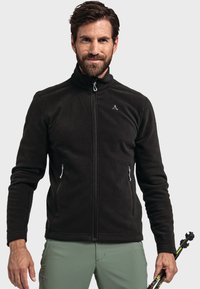 Chaqueta de forro polar negra con cuello alto, cierre de cremallera frontal y dos bolsillos laterales. Presenta un pequeño logo en el pecho. Textura suave.