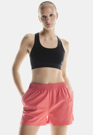 Sujetador deportivo negro con tirantes gruesos y banda ancha, combinado con pantalones cortos de cintura elástica en color coral que cuentan con bolsillos laterales y un diseño con abertura.