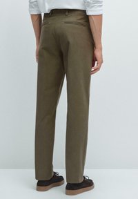Pantalons vert olive avec une coupe droite, poches doubles à l'arrière, et détails de couture subtils, associés à des chaussures marron foncé.
