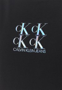 Svart t-shirt med en glansig, färgglad logo som har upprepade "cK" och texten "CALVIN KLEIN JEANS", centrerad design, slät tygstruktur.