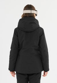 Svart skidjacka med en åtsittande huva, slät textur och justerbara ärmslut. Bakview visar en minimalistisk design och strömlinjeformad silhuett.